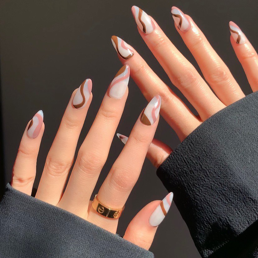 Two hands with long, almond-shaped nails featuring a white and brown wavy design, against a grey background.