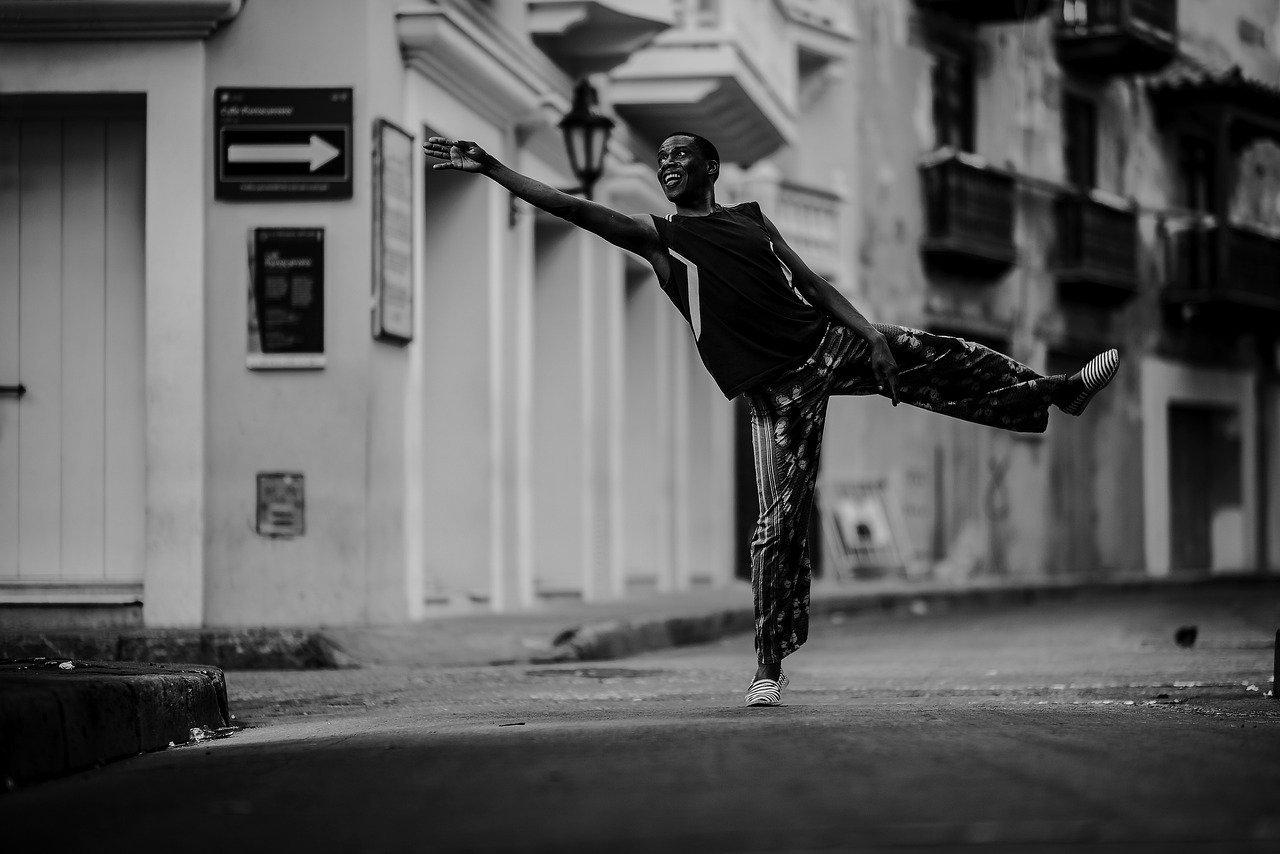 A black and white image of a person stretching out in front of a row of buildings. 