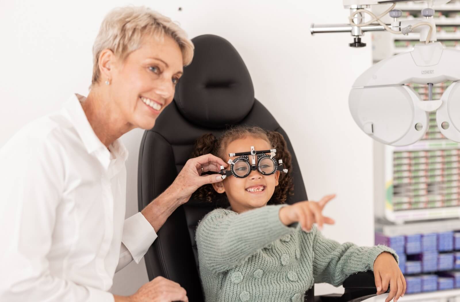 A young patient smiling as they undergo an eye exam, wearing trial frames as their optometrist assists them.