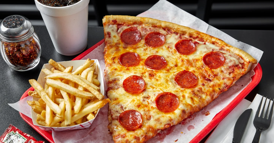 (A giant slice of pepperoni pizza served with golden fries and a soft drink on a red tray, creating a classic, satisfying fast-casual meal.)