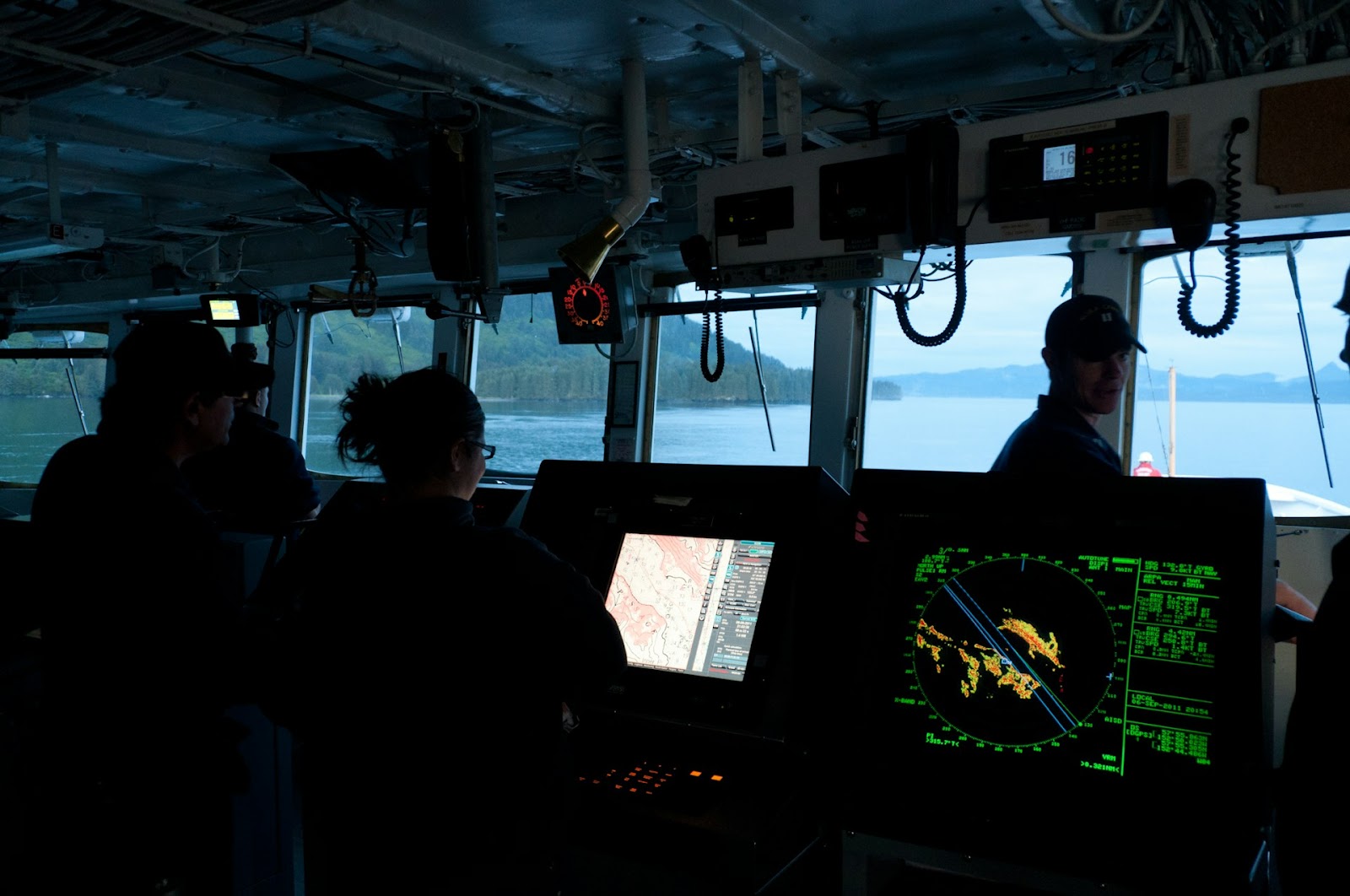 A group of people operates the bridge of a ship, with their attention focused on various navigation and control equipment.