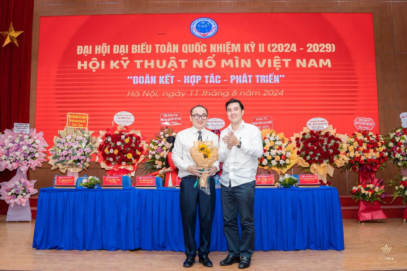 Two men standing in front of a red banner

Description automatically generated