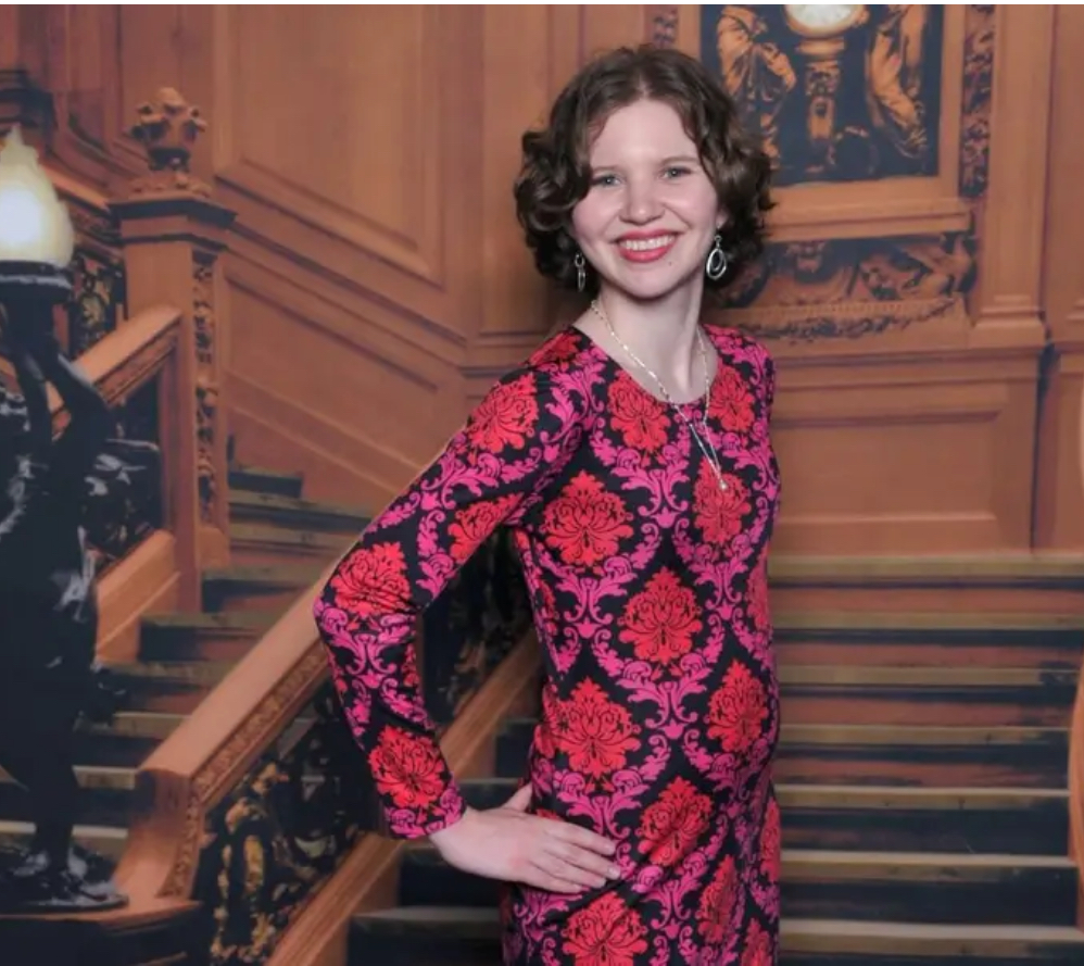 A woman smiling in a brightly colored dress on a staircase. 