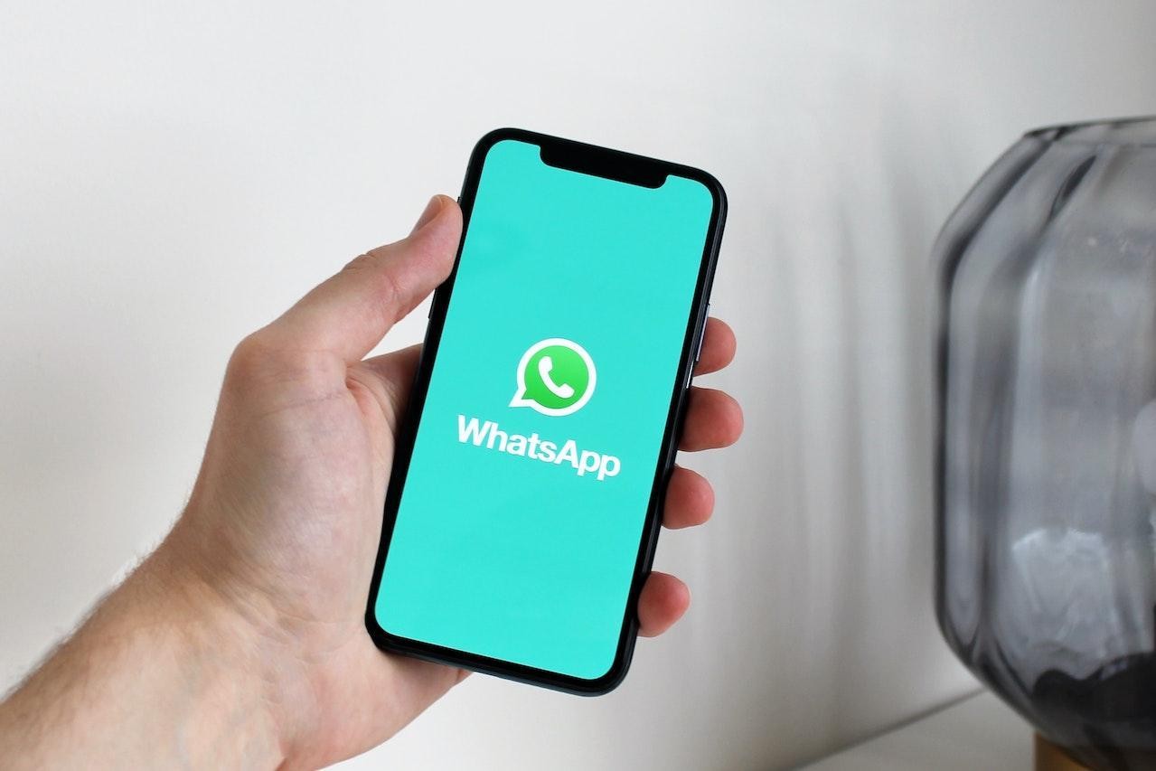 tangan kiri seseorang menggenggam sebuah iphone yang membuka aplikasi WhatsApp