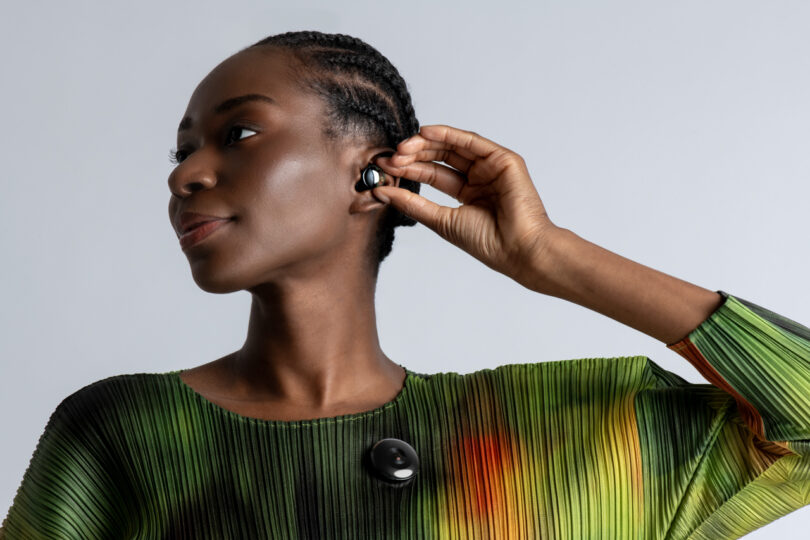 Person wearing a green and orange pleated top adjusts in-ear wireless headphones while looking to the side.