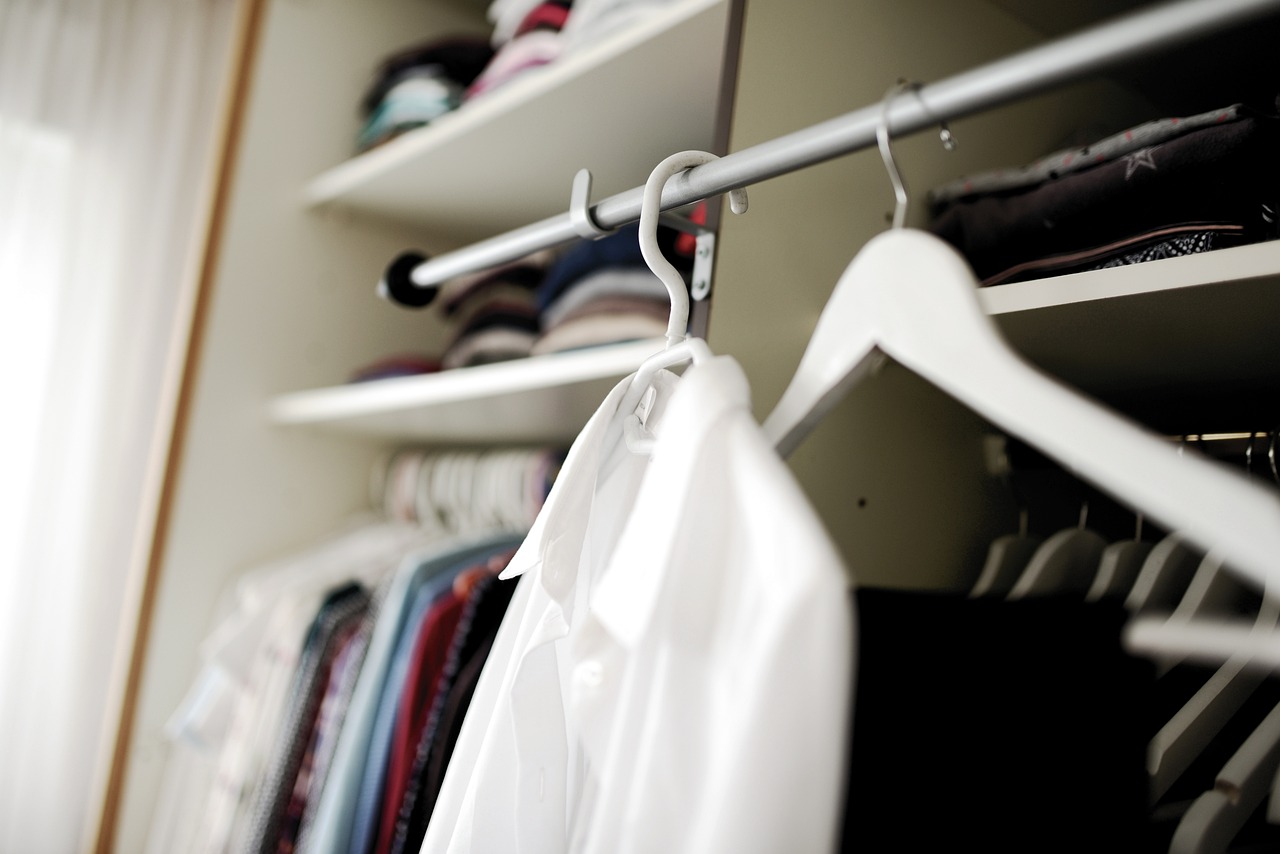 A white button up shirt ihanging in a closet. Othering clothing in the background. 