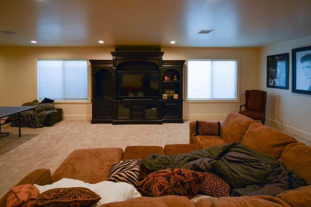 The basement is filled with an L-shaped sectional, a TV, and a wingback chair over carpet flooring.