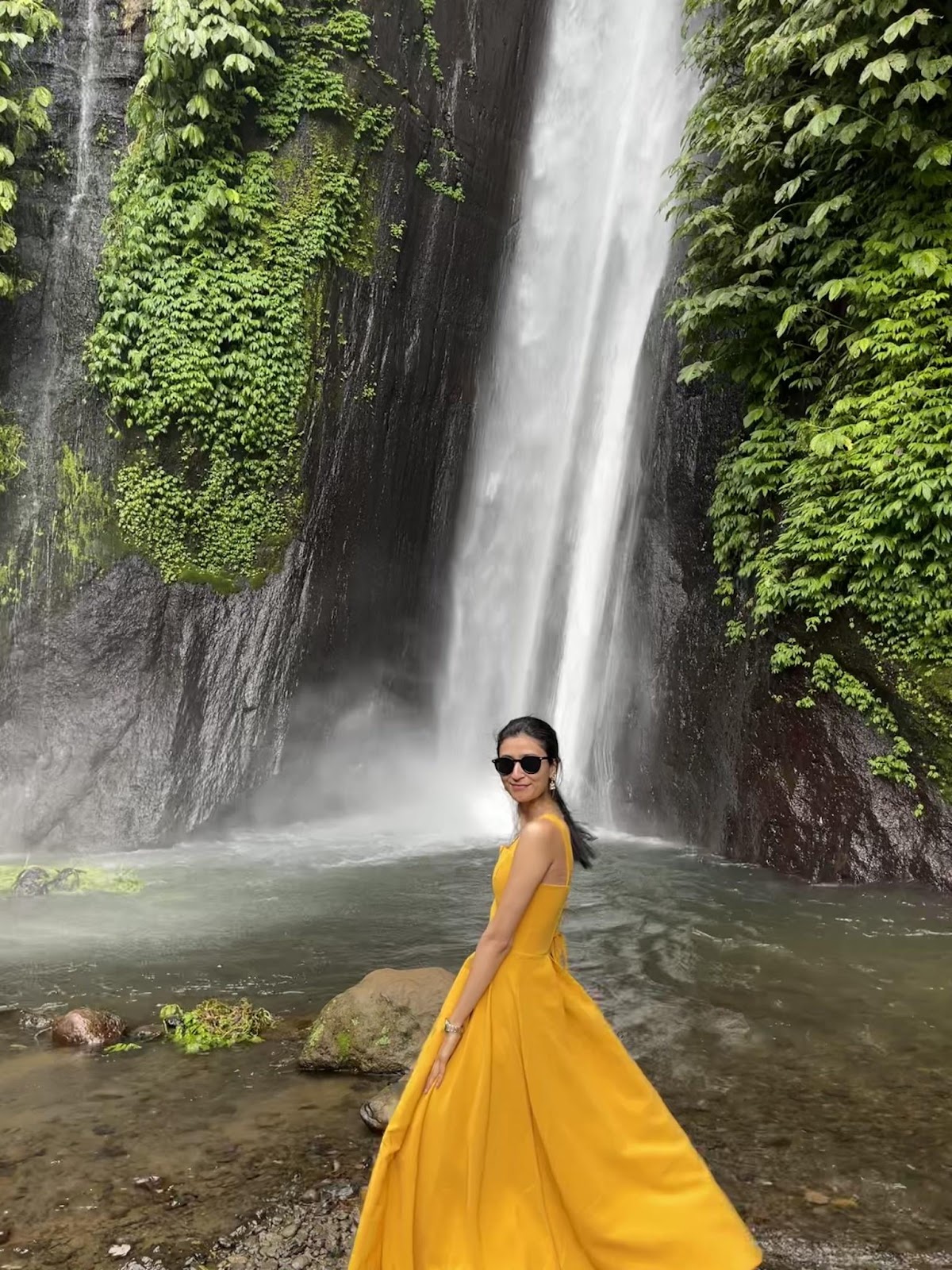 a girl standing in front of a large waterfall in north bali