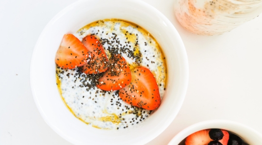 Un bol de pouding au chia garni de tranches de fraises fraîches et de graines de chia, accompagné d'un bol de baies mélangées.