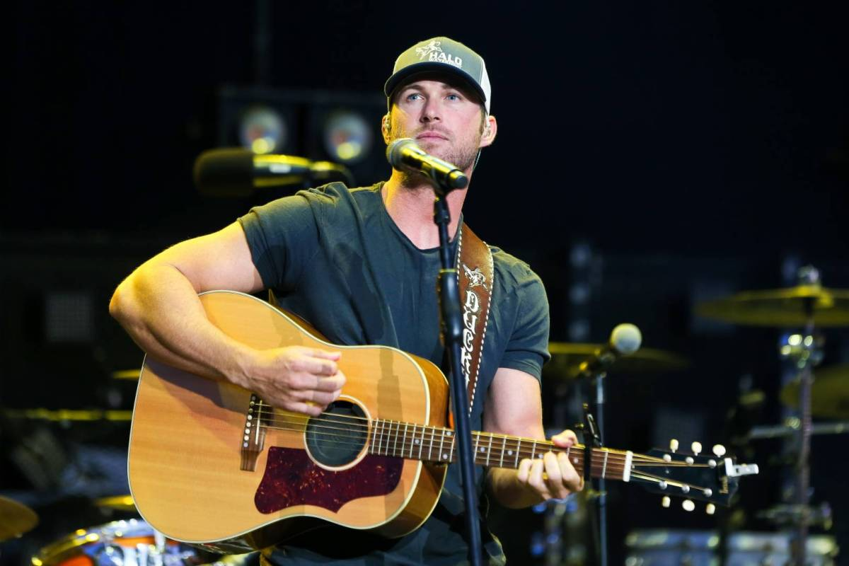 A white man in a tee and baseball cap plays guitar on stage