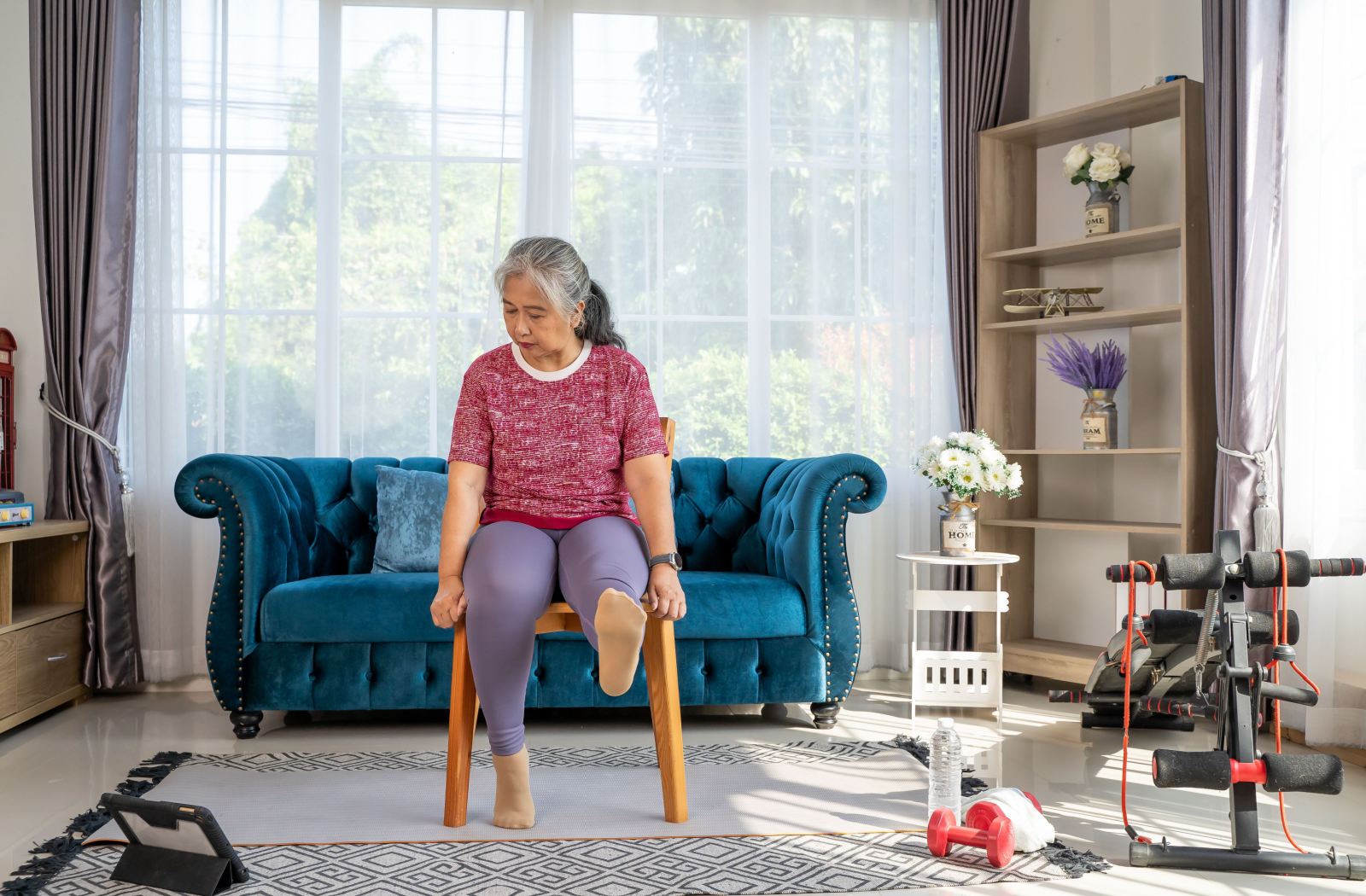 A senior sits atop a wooden stool, exercising their legs.