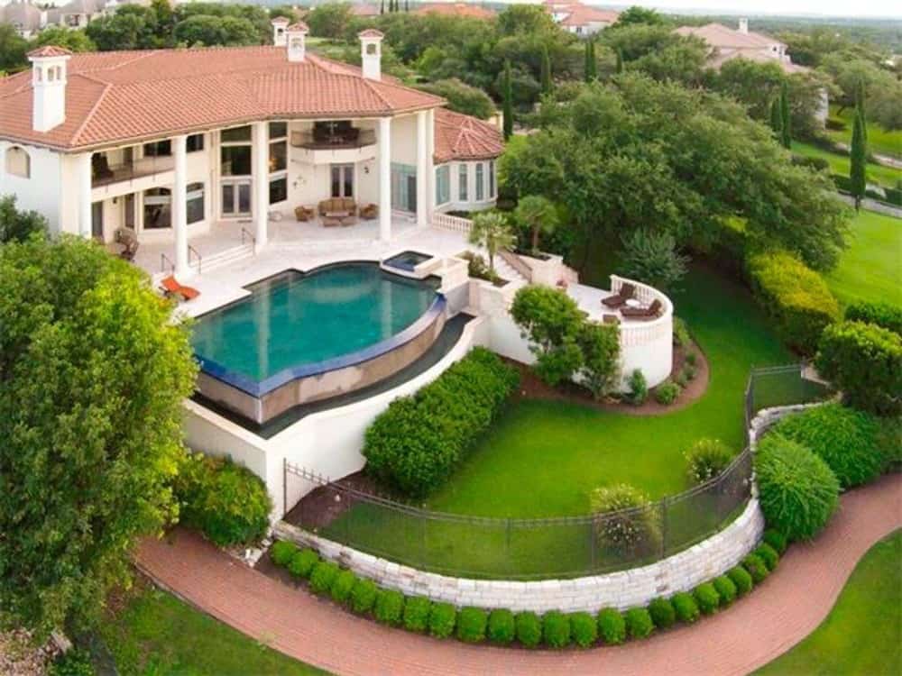 Aerial view of the house showing its lush green lawn, a swimming pool, upper balconies, and covered porches.Aerial view of the house showing its lush green lawn, a swimming pool, upper balconies, and covered porches.