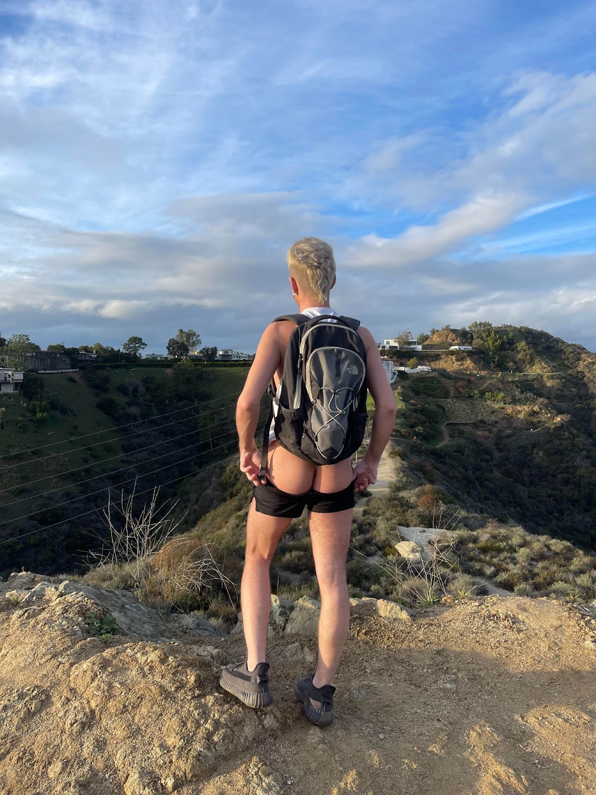 gay xxx onlyfans content creator Dallas Knoxxx standing on a california hikinh trail showing off his gay bubble butt with his black running shorts pulled down