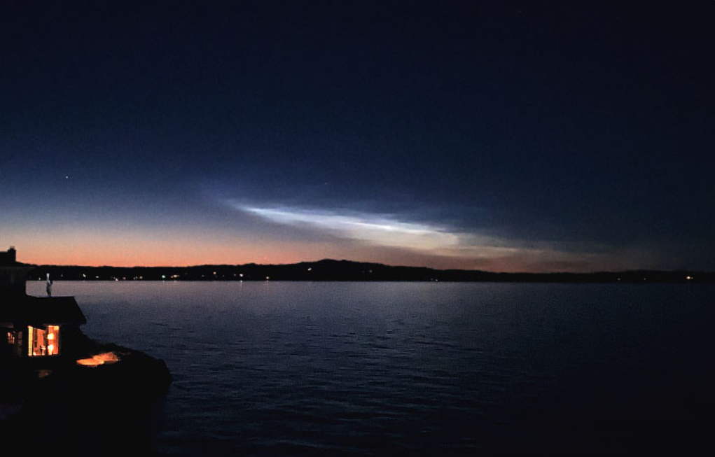 Night photo, the sky is dark but some wispy shiny cloud is near the horizon.