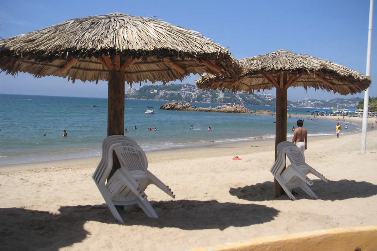 Chairs are kept under the shade and people are enjoying on the beach
