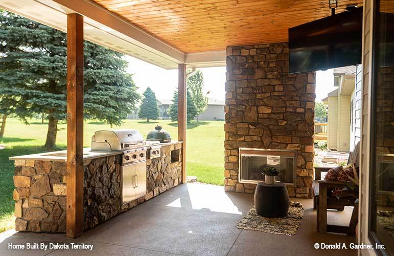 Rear patio with a large stone fireplace and a summer kitchen lined with wooden posts.
