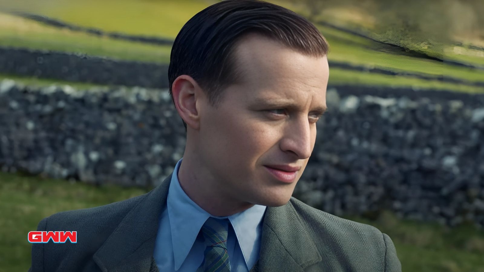 James Herriot looks contemplative standing against a stone wall.