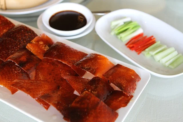 in one dish cooked peking duck, and in other dish vegies are placed. and in other bowl soya sauce is present