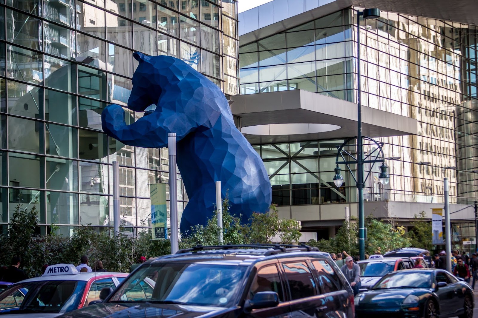 The front of the Colorado Convention Center with people, cars, and taxi