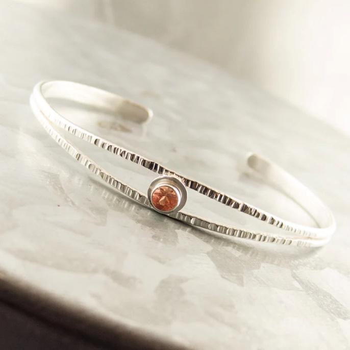 A silver bracelet with a round stone in the center

Description automatically generated