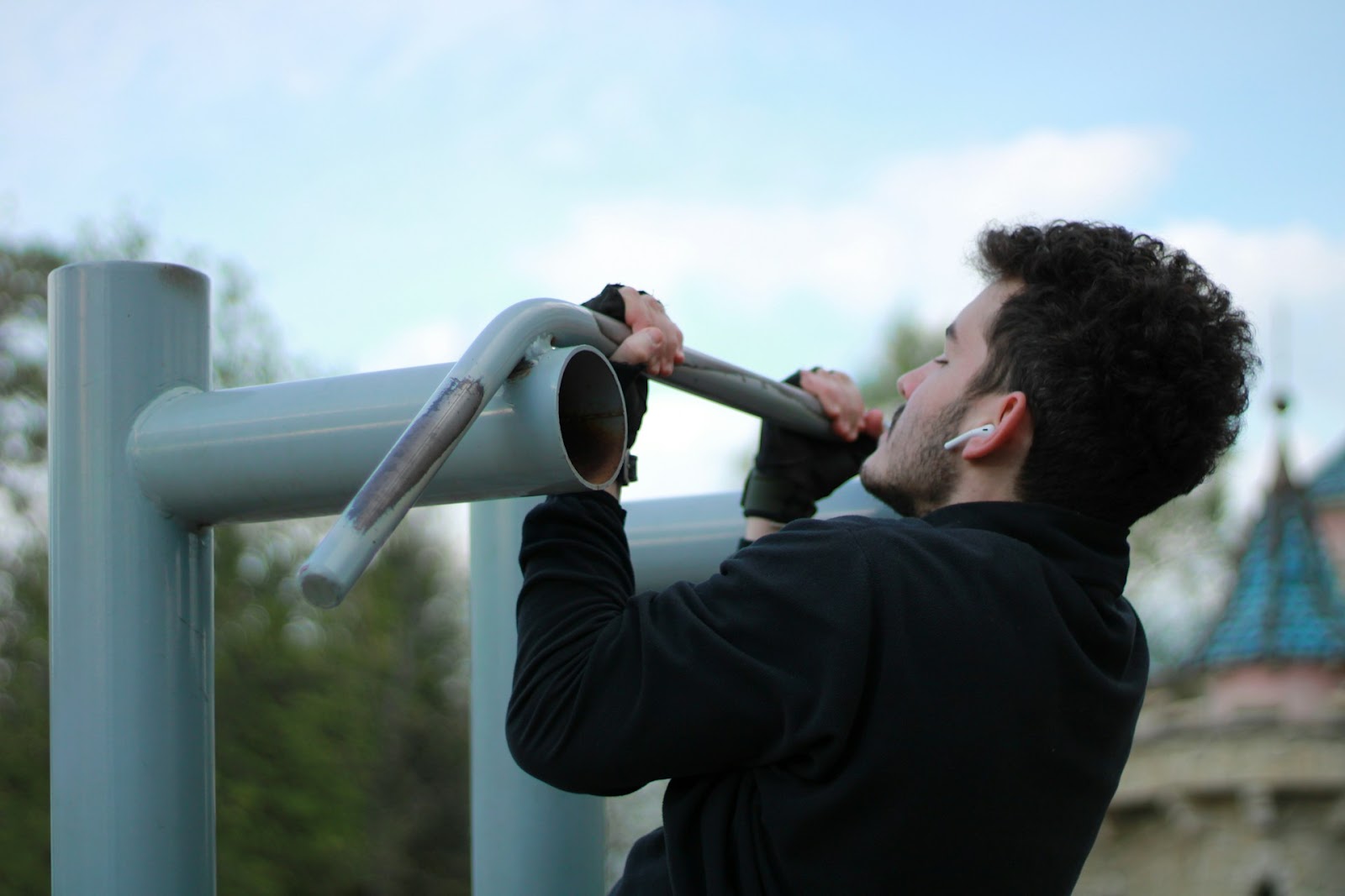 A man in a black jacket doing a chin up on a metal pole.