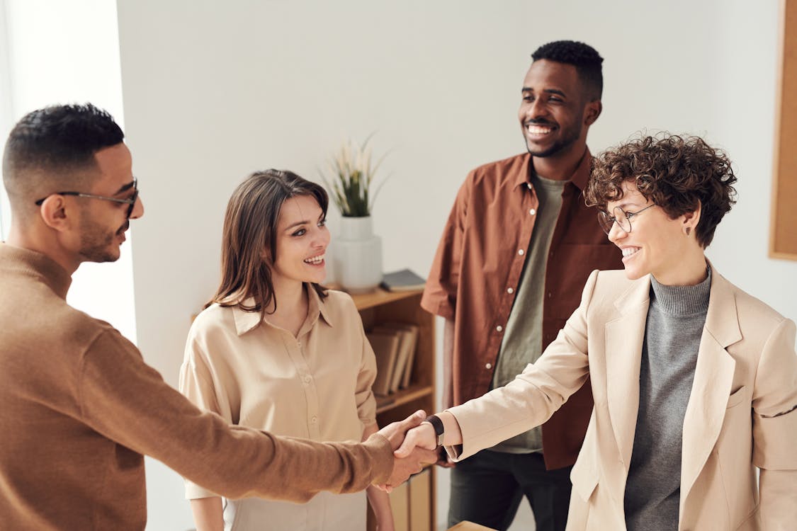 Free Four colleagues smiling and shaking hands in a bright office setting. Stock Photo