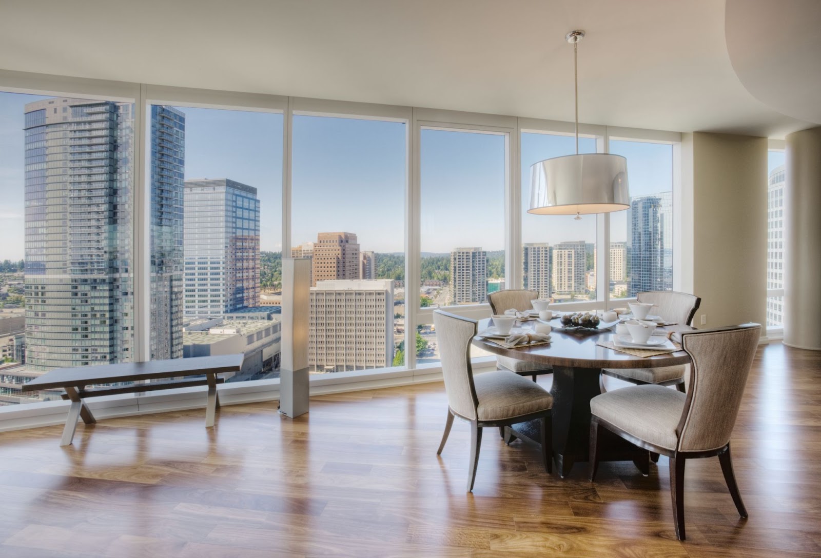 Dining area in a luxury high-rise apartment in Uptown Dallas, featuring floor-to-ceiling windows with a panoramic view of skyscrapers and the city skyline. Elegant wooden flooring and contemporary dining furniture.