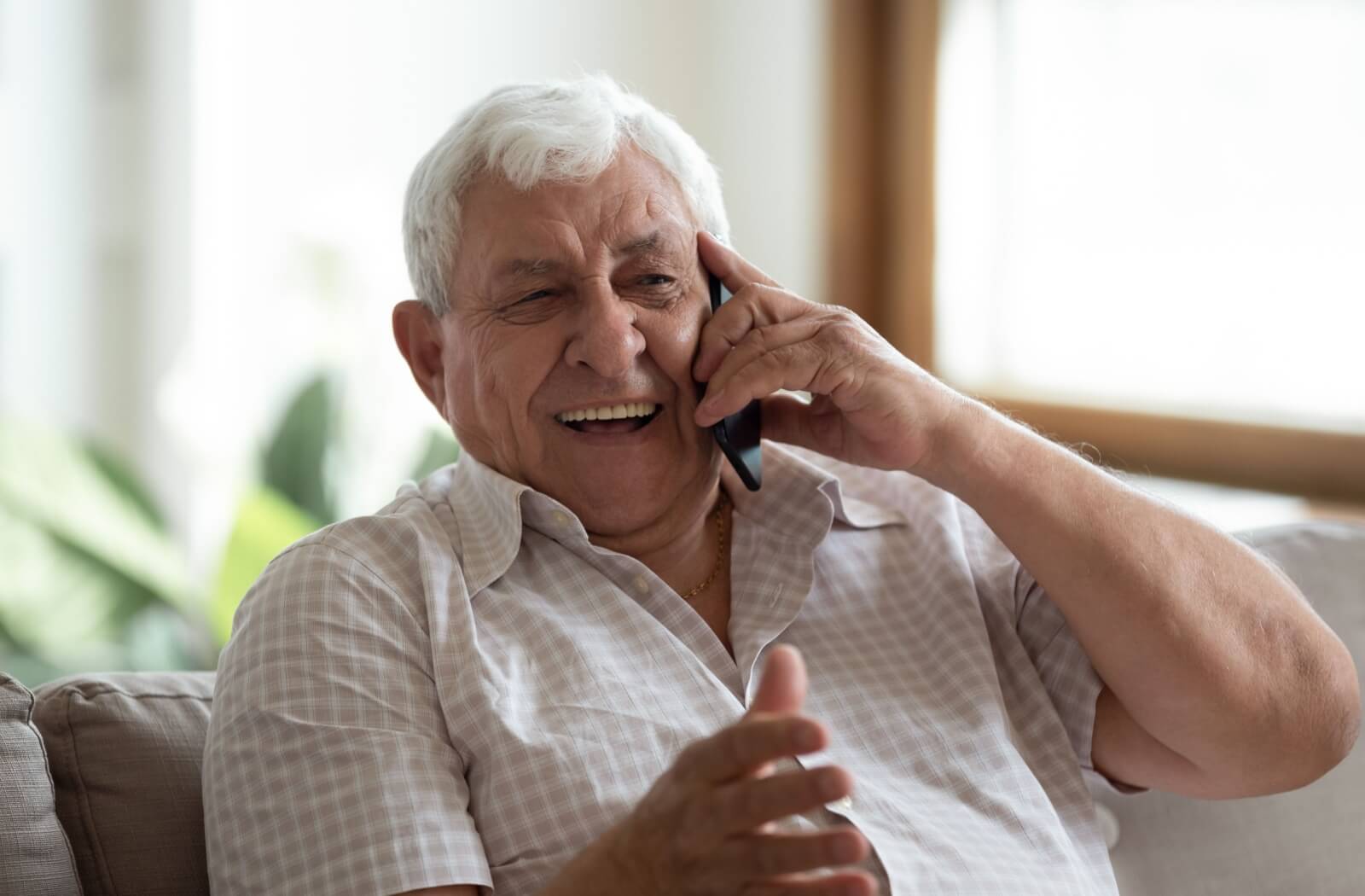 A senior with dementia laughs while talking on the phone with their loved one.