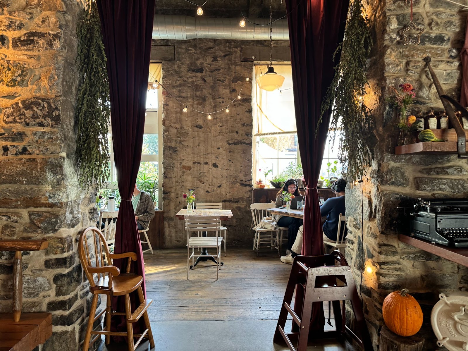 Inside of a rustic-looking coffee shop with fall decor and people sitting at small, white tables.