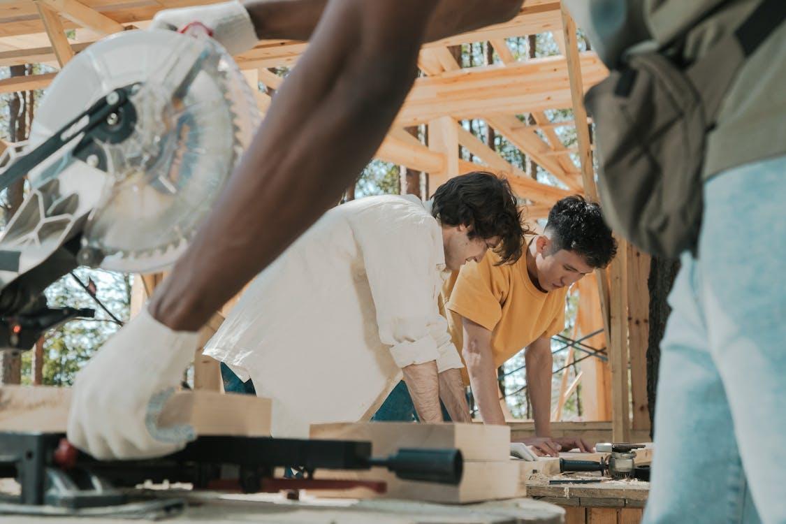 Free Workers using a circular saw on a sunny day at an outdoor construction site, collaborating on carpentry work. Stock Photo