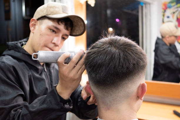 A barbering student practicing haircutting techniques under the guidance of a professional instructor.