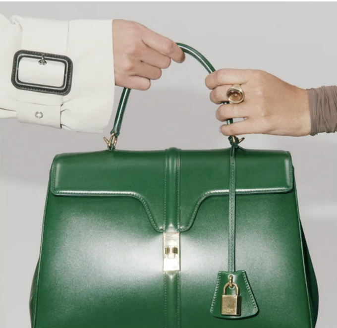 Two hands holding a green luxury handbag with gold hardware, symbolizing a transaction or exchange.