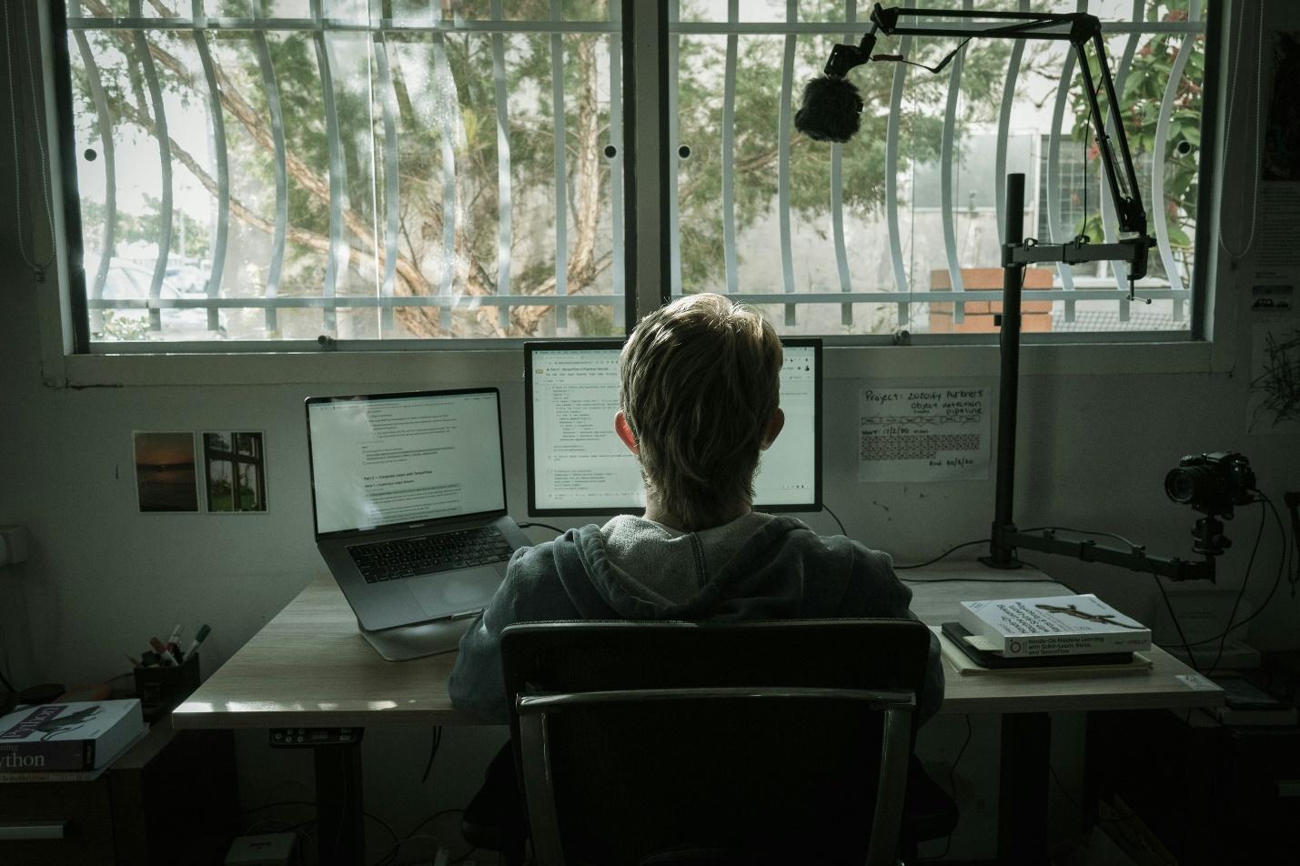 person in gray hoodie sitting on chair in front of laptop computer