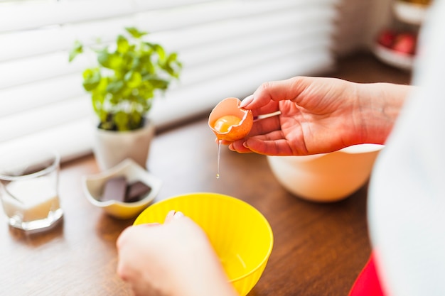 Crop woman putting raw eggs into bowl