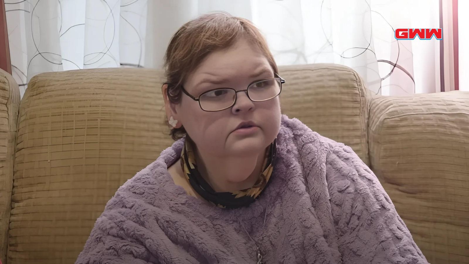 Tammy in glasses and purple shawl sitting on a couch, looking concerned.