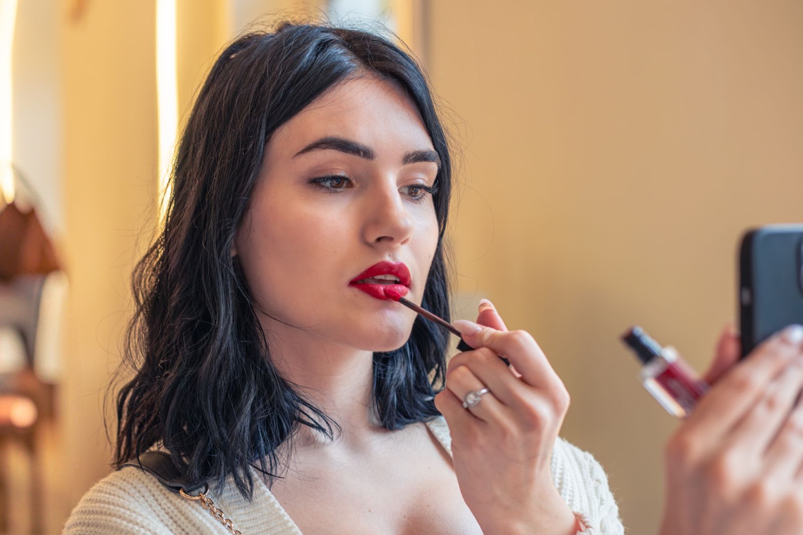 A woman applying lipstick while looking at her phone camera