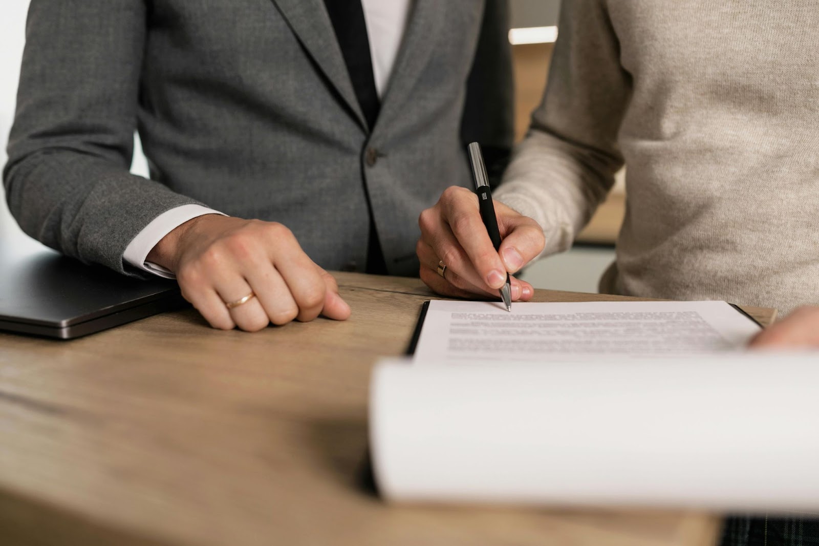 A man signs a contract while another man stands near him.