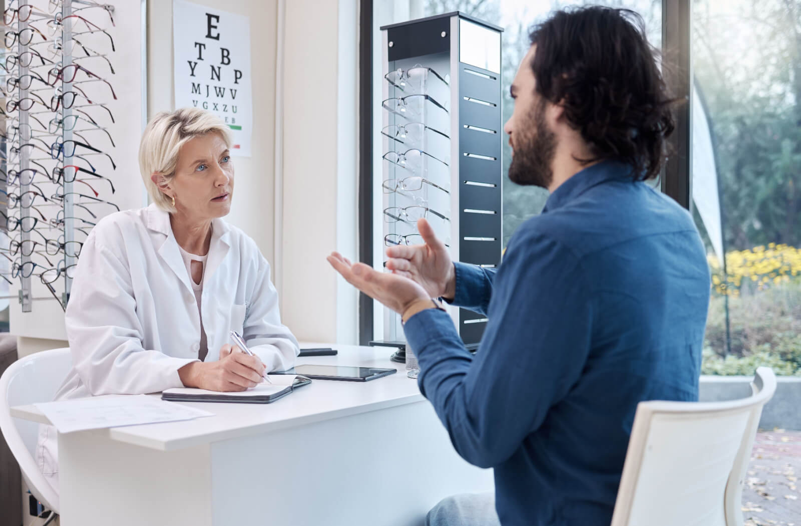 An optometrist listening patiently while her patient describes the symptoms of his meibomian gland dysfunction.