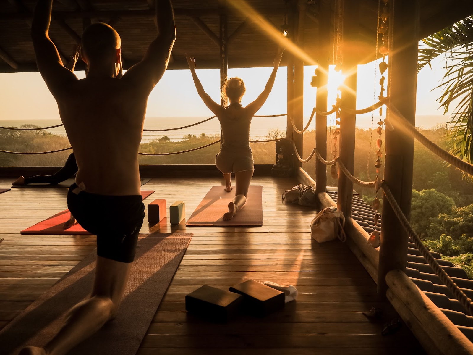 A wellness retreat in Santa Teresa, Costa Rica, with guests practicing yoga on a wooden deck overlooking the ocean at sunrise, embodying mindful escapes and eco-luxury travel.