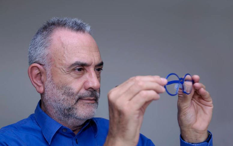 Man in blue shirt looking into the lens of his glasses for spots