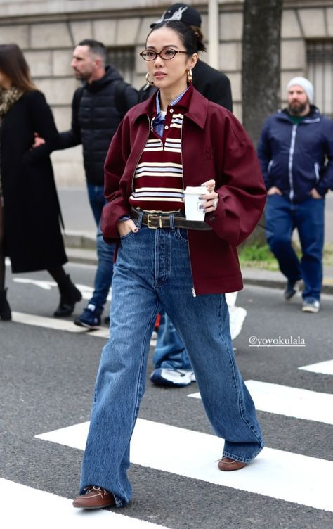 wanita menyeberang zebra cross memakai celana jeans biru, kaos bergaris, dan jaket burgundy