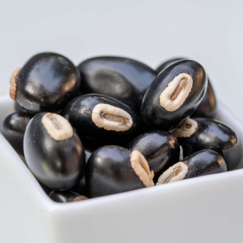 A white bowl filled with black beans, representing Mucuna Pruriens, or Velvet Bean.