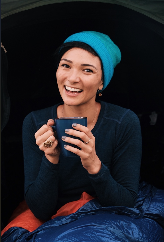 Woman wearing Merino wool base layer and beanie, enjoying warmth in a tent during winter camping
