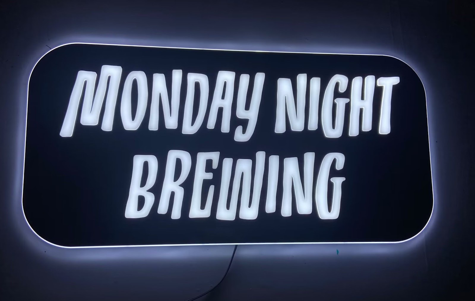 a LED sign with white text that reads "Monday Night Brewing"