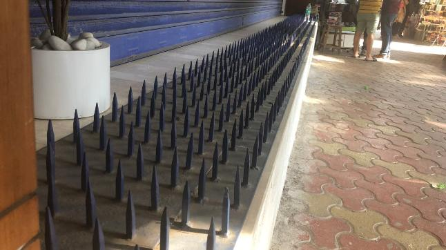 A row of black metal spikes, an example of hostile architecture, is installed on a concrete ledge outside a building to prevent sitting or loitering.