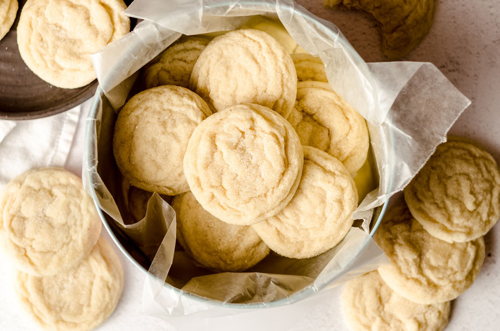 Top view of sugar cookies in a paper-lined container, displayed on a light surface