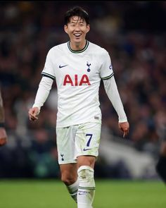 This contain Son Heung Min  is smiling and walking on the field with his foot in the air