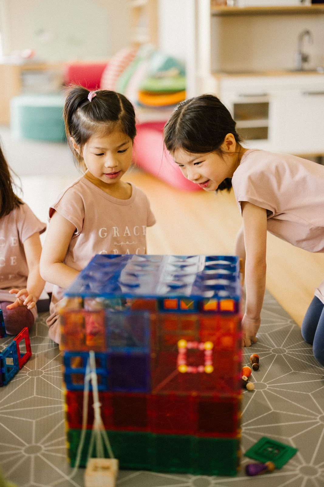 Two sibling girls are playing with magnetic tiles, using the tiles as structures and props for their storytelling scene. They creatively arrange the colorful tiles to build settings for their imaginative narrative, using peg dolls as people to bring their vibrant story to life through playful and engaging interactions.
