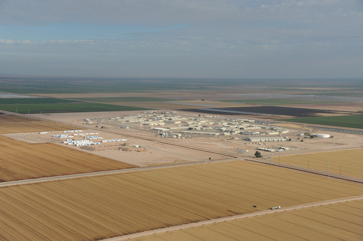 An aerial view of Calipatria State Prison, a cluster of low tan buildings on a flat landscape of fields.