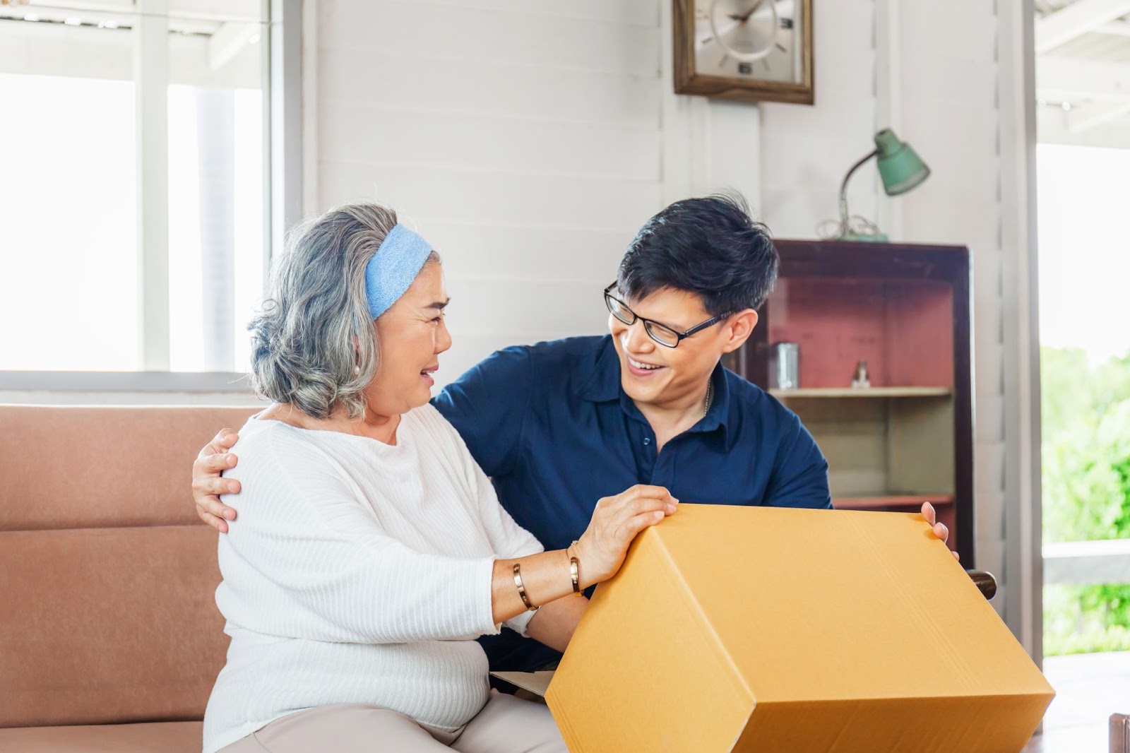 An adult son helping his older adult mother move into a memory care community with personal things from her home.